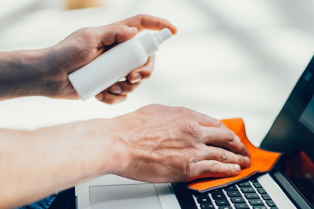 Close up. man spraying spray on the surface of a laptop . concept of health protection