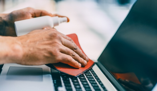 Photo close up. man spraying spray on the surface of a laptop . concept of health protection