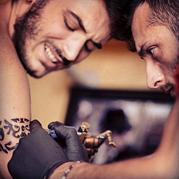 Photo close-up of man tattooing on customer arm