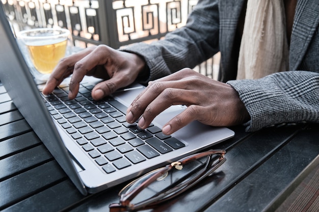 Close-up of man typing on laptop computer while sitting at the table outdoors