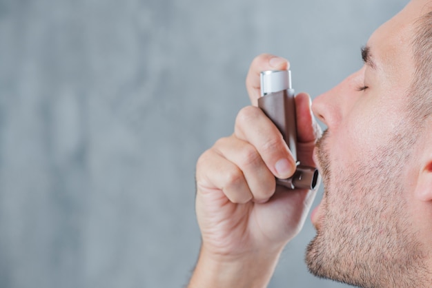 Close-up of a man using asthma inhaler against blur backdrop