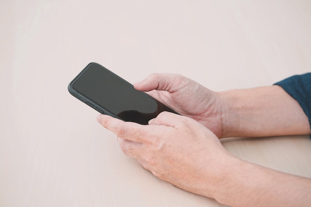 Close up of a man using mobile smart phone on wood table.