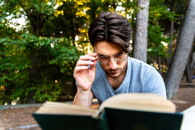 Foto close-up di un uomo che indossa occhiali che legge un libro al parco