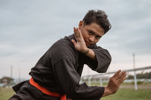 Close up of a man wearing a pencak silat uniform with a pasang motion in nature