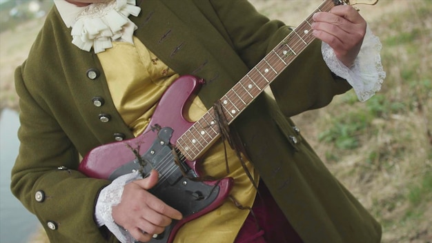 Close up for man with a purple electric guitar playing in old fashioned costume of rococo manner on