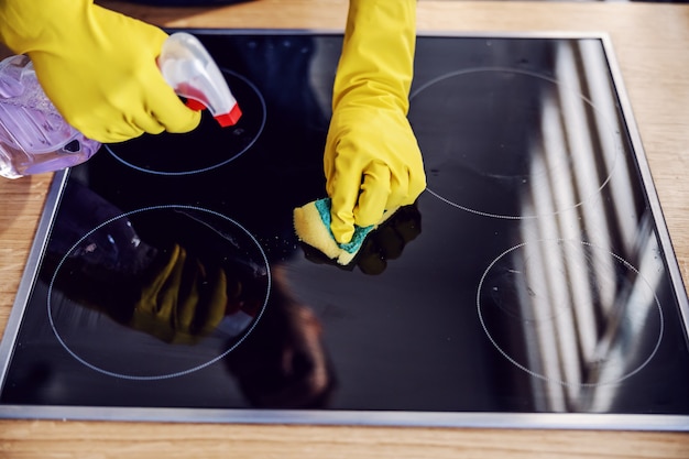 Close up of man with rubber gloves cleaning with sprayer and sponge very dirty stove.