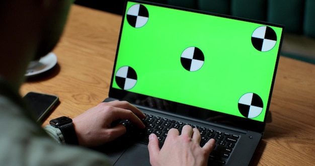 Close up of man working on laptop with green screen in coffee shop