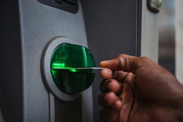 은행 계좌에 현금을 입금하기 위해 ATM에 신용 카드를 삽입하는 사람의 손 클로즈업