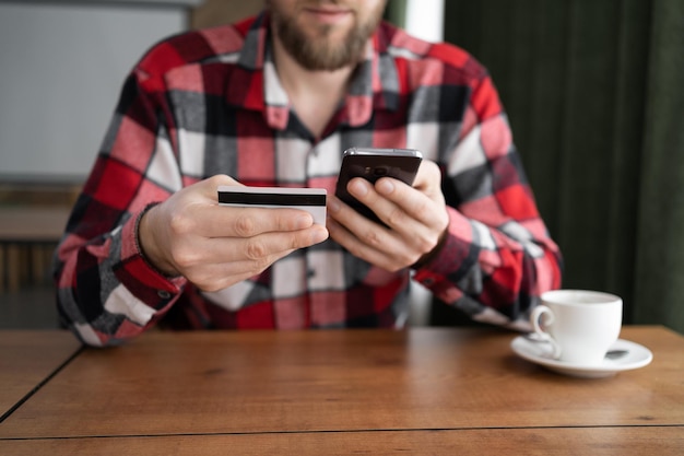 Close-up mannelijke handen met een mobiele telefoon tikken kaartgegevens om een online betaling te maken terwijl ze in een café zitten met een creditcard en een telefoon die betaalt voor online aankopen