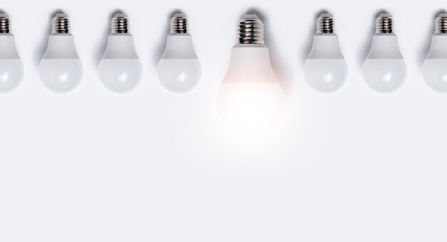 Photo close-up of many light bulbs with one glowing against white background. business idea concept with copy space.