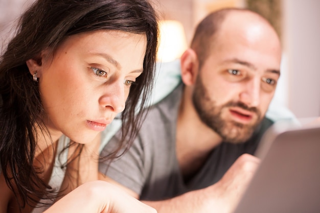 Photo close up of married young couple wearing pajamas using laptop for shopping during quarantine.