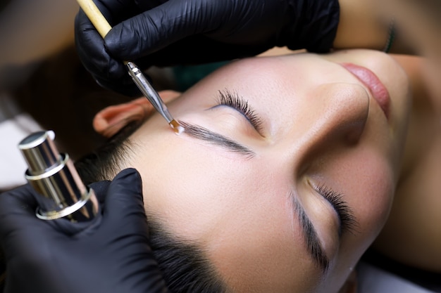 Photo close-up of the master combs the eyebrows of the model with a brush after the procedure of long-term eyebrow styling