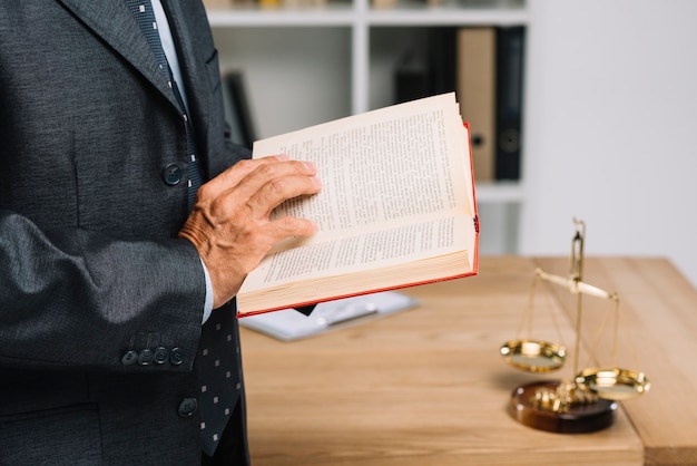 Photo close-up of mature lawyer reading law book in the courtroom