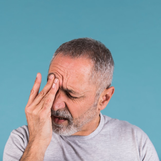 close-up of a mature man suffering from headache on blue background