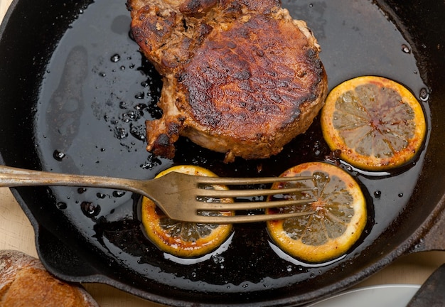 Photo close-up of meat with lemon slices on frying pan at table