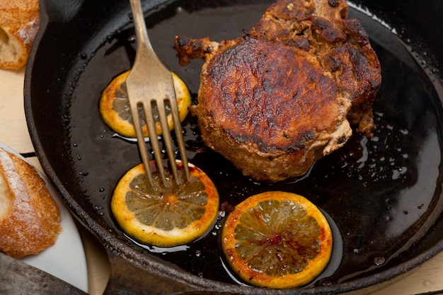 Photo close-up of meat with lemon slices on frying pan at table