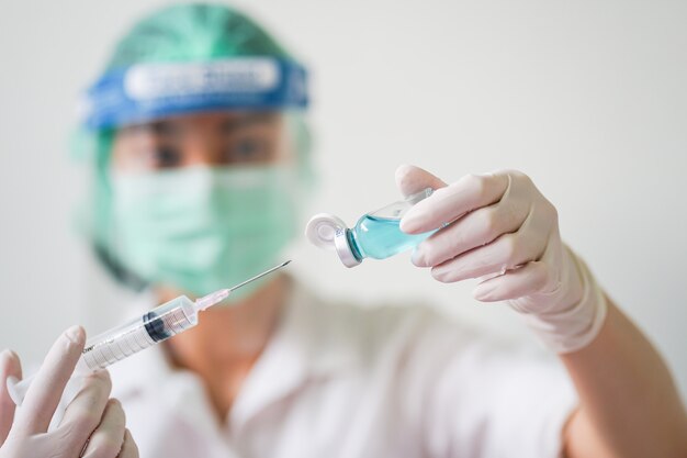 Photo close up medical doctor wearing face shield, medical mask and medical grove. she holding draw syringe and bottle with coronavirus vaccine for 2019-ncov covid virus.