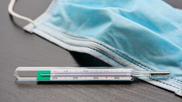 Close-up of medical protective mask and thermometer on black