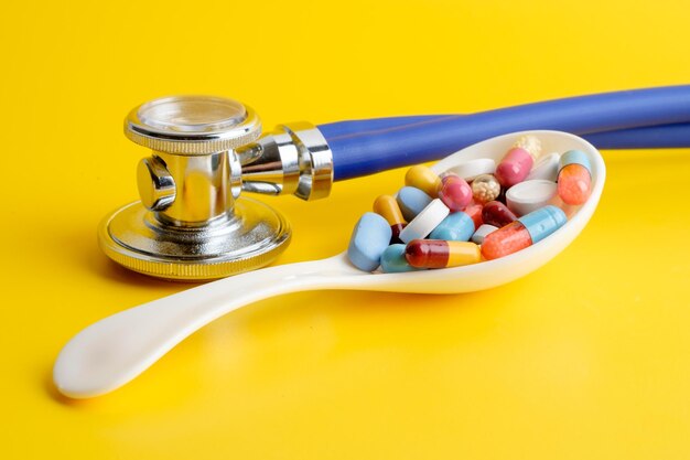 Close-up of medicines in spoon by stethoscope over yellow background