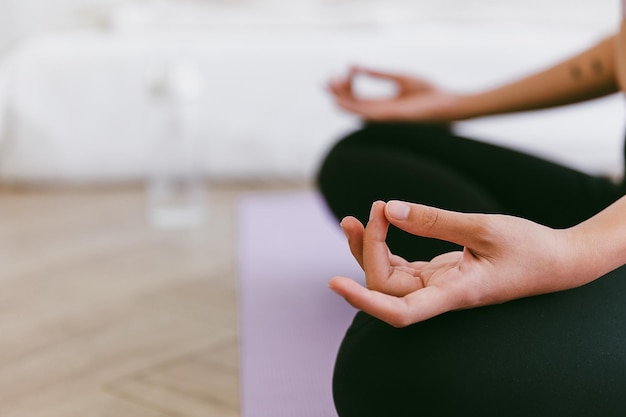 Close up of meditation hand of sporty Asian woman practicing yoga on yoga mat doing Ardha Padmasana exercise meditating in Half Lotus pose indoor working out at home