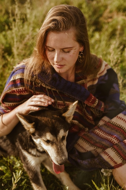 Foto close-up meisje in ethno cape met natuurlijke schoonheid zonder make-up streelt de honden hand zit in de g