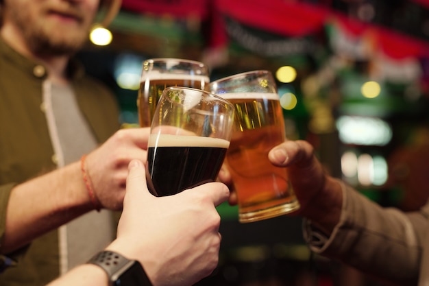 Close-up of men holding glasses of beer and toasting during their meeting in the bar