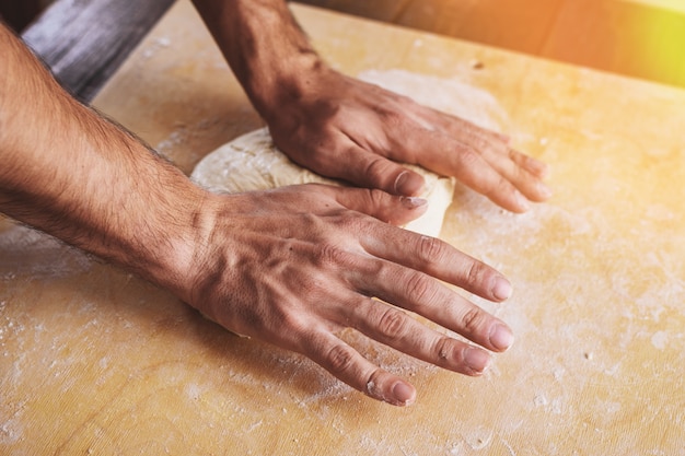 Il primo piano delle mani degli uomini si stende, prepara la base per la pizza.