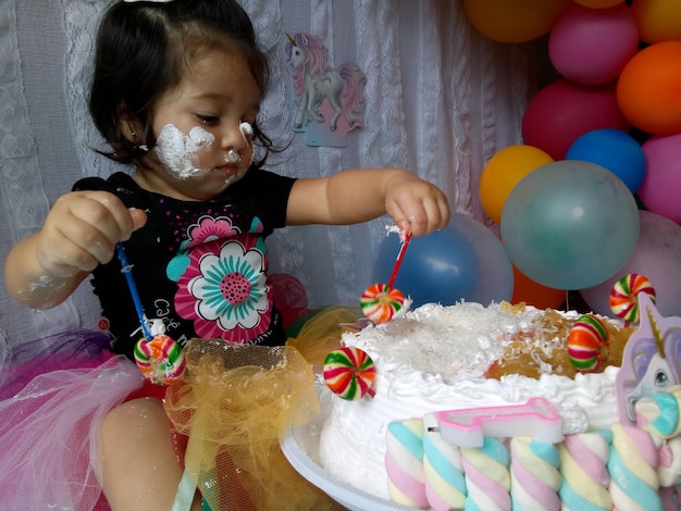 Photo close-up of messy baby girl eating cake at home during birthday