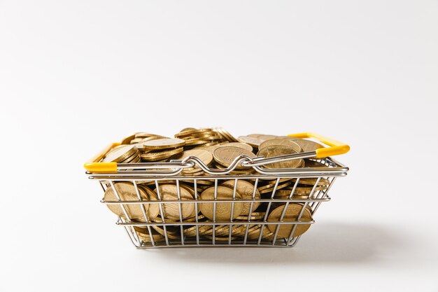 Close up of metal grocery basket for shopping in supermarket with lowered yellow handles filled with golden coins isolated on white background. Concept of shopping, money. Copy space for advertisement
