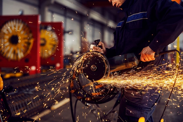 Close up of metallurgy worker grinding armature with a grinder in the facility