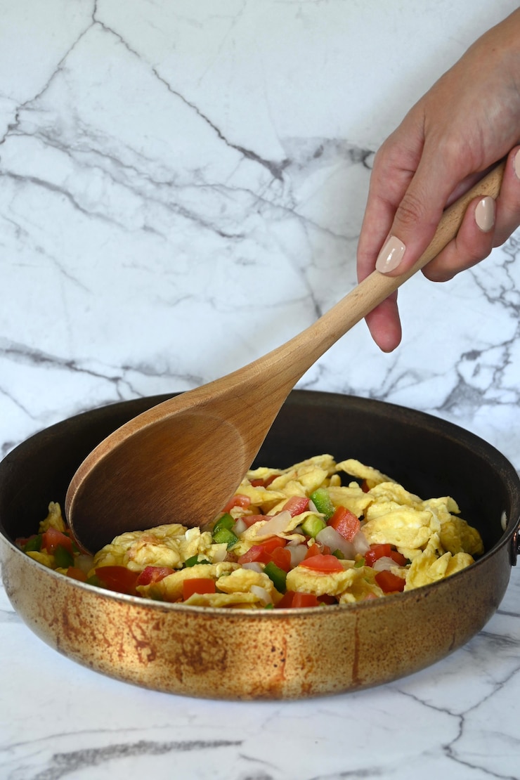 Close-up of Mexican eggs in frying pan, Latin young woman's hand, marble background, copy space