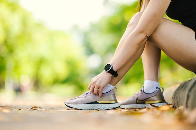 Primo piano di mezza età bella donna asiatica sportiva che si allaccia i lacci delle scarpe all'aperto in una bella giornata estiva.