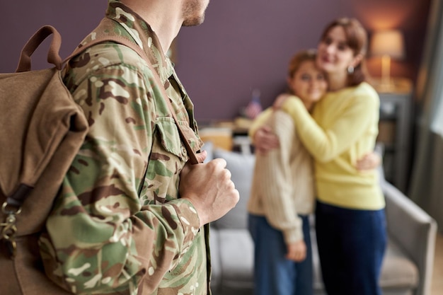 Close up of military man holding backpack looking at family in background