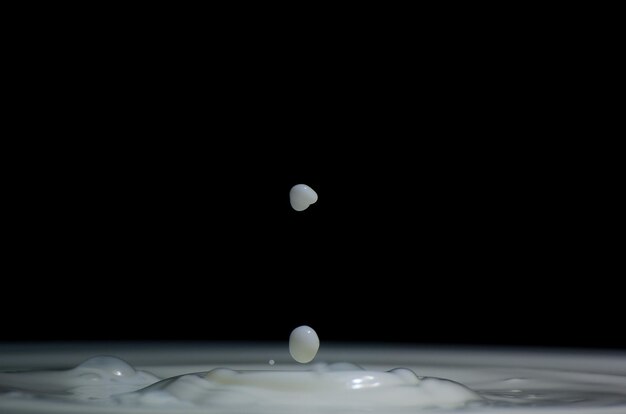 Photo close-up of milk drops falling against black background