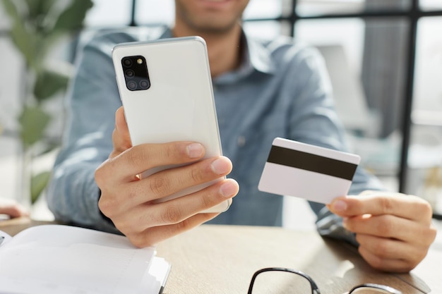 Close up millennial man holding smartphone and banking credit card