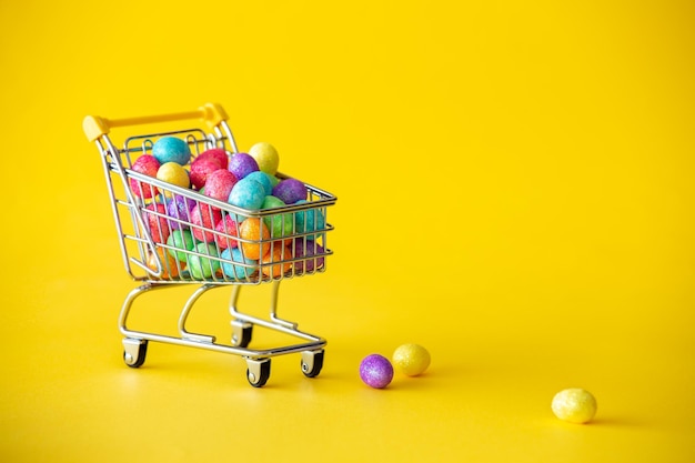 Close-up of miniature shopping cart against yellow background