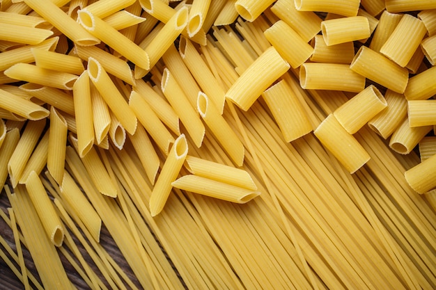 Close up mix of raw dried talian pasta, macaroni, spaghetti, penne on wooden table.  Top view