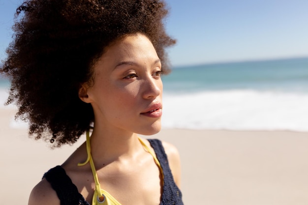 Close up of a mixed race woman with afro hairtsyle, on holiday, enjoying free time walking on a sunny beach, with blue sky and sea in the background