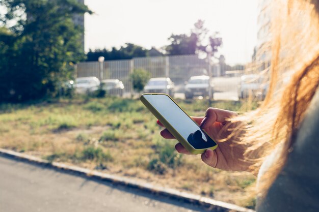 日光の下で街の背景に女性の手で携帯電話のクローズアップ