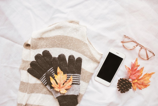 Close up of mobile phone with warm clothing on bed
