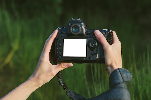 Close-up mock-up di una macchina fotografica professionale foto-video nelle mani di una ragazza. sullo sfondo della natura verde.