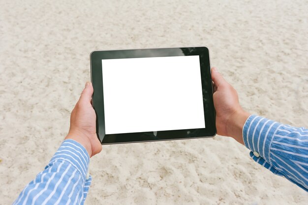 Закройте макет планшета в руках мужчины. На фоне пляжа и песка.
