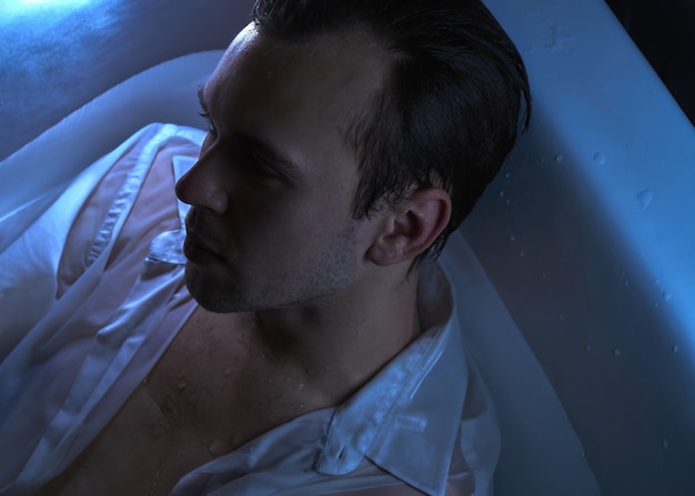 Close-up mode portret van blanke knappe ongeschoren man in de badkamer in sexy nat wit overhemd op zoek naar de kant sterk gezicht