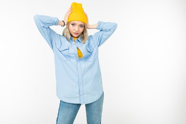 Close-up of a model girl in a stylish denim shirt with a blonde haircut on a white studio background.