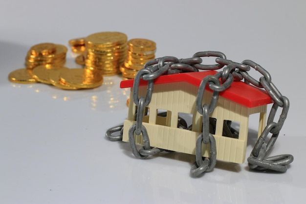 Photo close-up of model home with chain against coins and white background