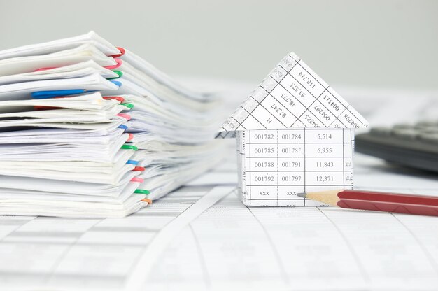Photo close-up of model house with pencil files on financial documents against gray background