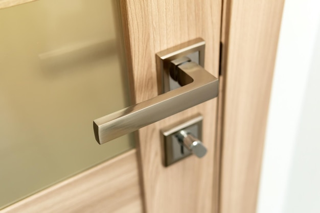 Close-up of a modern chrome metal door handle on wooden door.