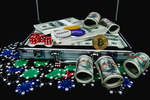 Close-up of money with gambling chips and dice by briefcase against black background