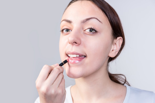 Close-up mooie jonge vrouw lippenstift make-up toe te passen tijdens het kijken naar de camera op een witte achtergrond.