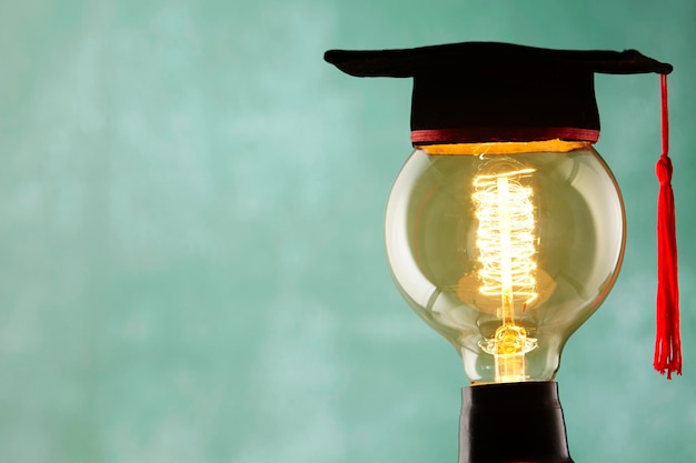 Photo close-up of mortarboard on illuminated light bulb against blue background